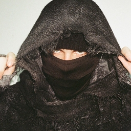 Frustrated Finn in a dark hooded scarf and face mask, looking at the camera